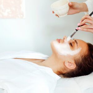 Crop cosmetologist applying facial mask on client